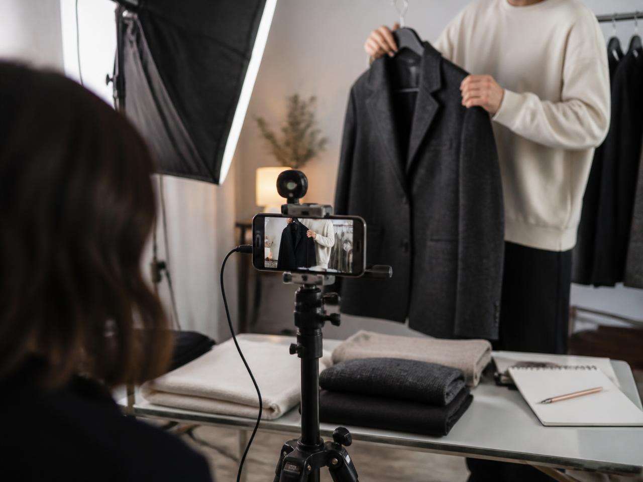 A phone on a tripod filming a wool coat being held up in a working studio